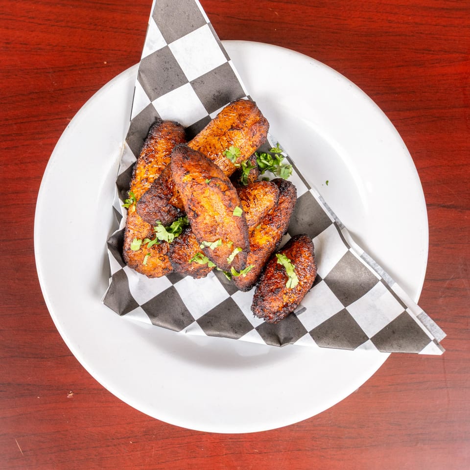 Grilled, spice-crusted chicken pieces garnished with fresh herbs on checkered paper atop a white plate.
