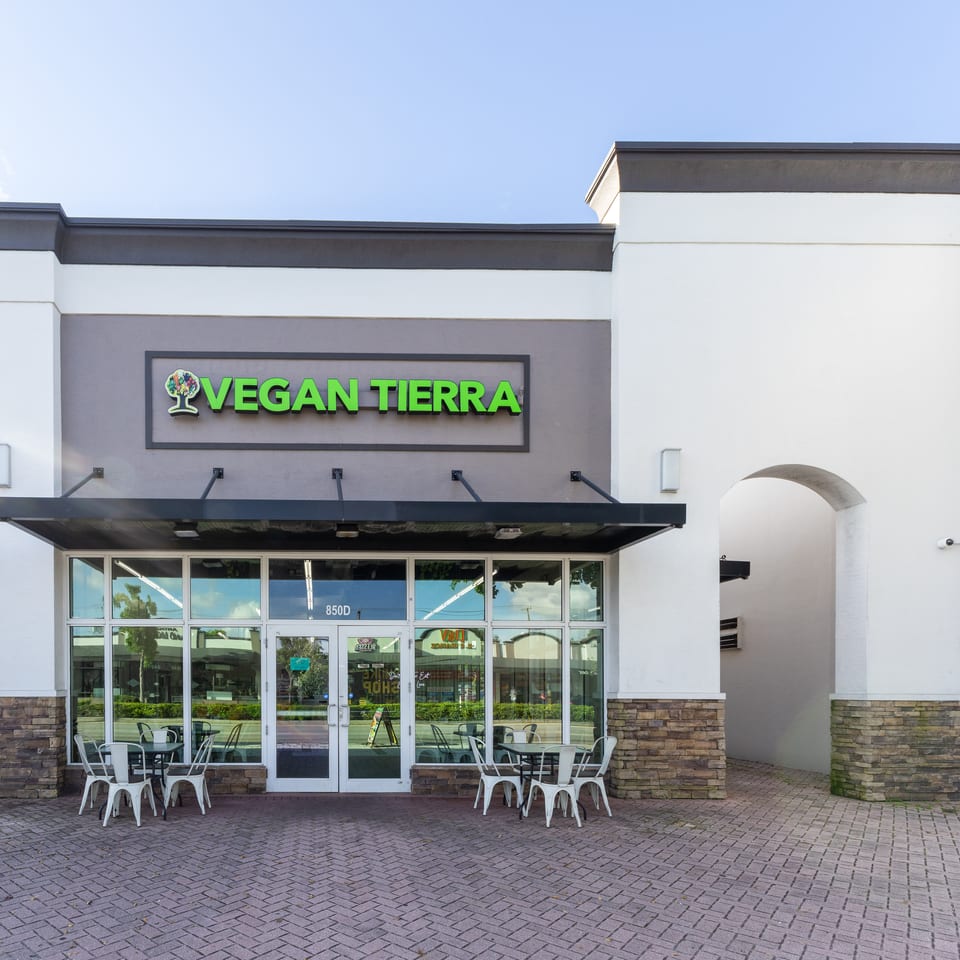 Vegan Tierra restaurant storefront with green signage, glass entrance, outdoor tables, and white stucco architecture.