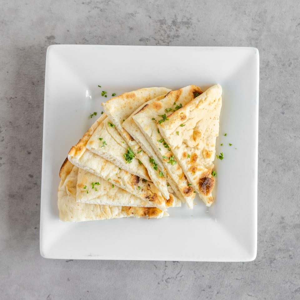 Grilled pita bread triangles garnished with chopped parsley on a white square plate.