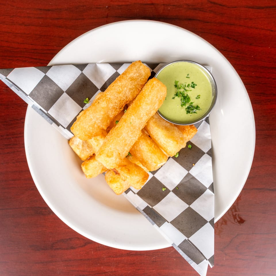 Crispy golden fried rolls served on checkered paper with a bowl of green herb dipping sauce.