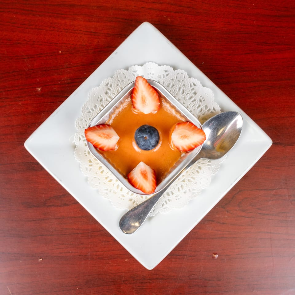 Caramel dessert topped with sliced strawberries and a blueberry, served in a square dish with a spoon.