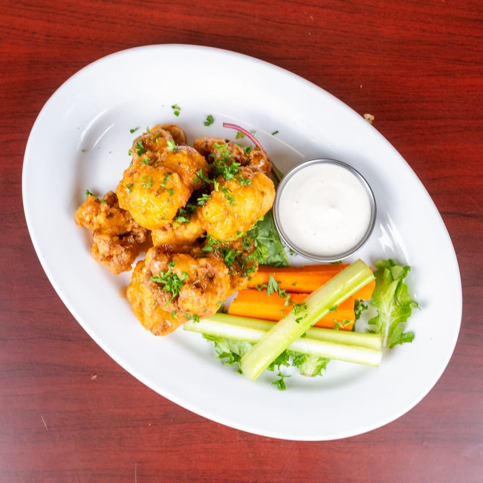 Plate of crispy fried chicken pieces garnished with parsley, served with ranch dipping sauce, carrots, celery, and lettuce.