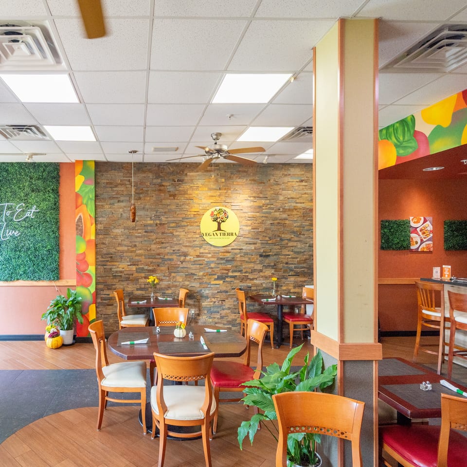 Bright Vegan Tierra restaurant dining room with colorful fruit murals, greenery, stone accent wall, and neatly arranged tables and chairs.
