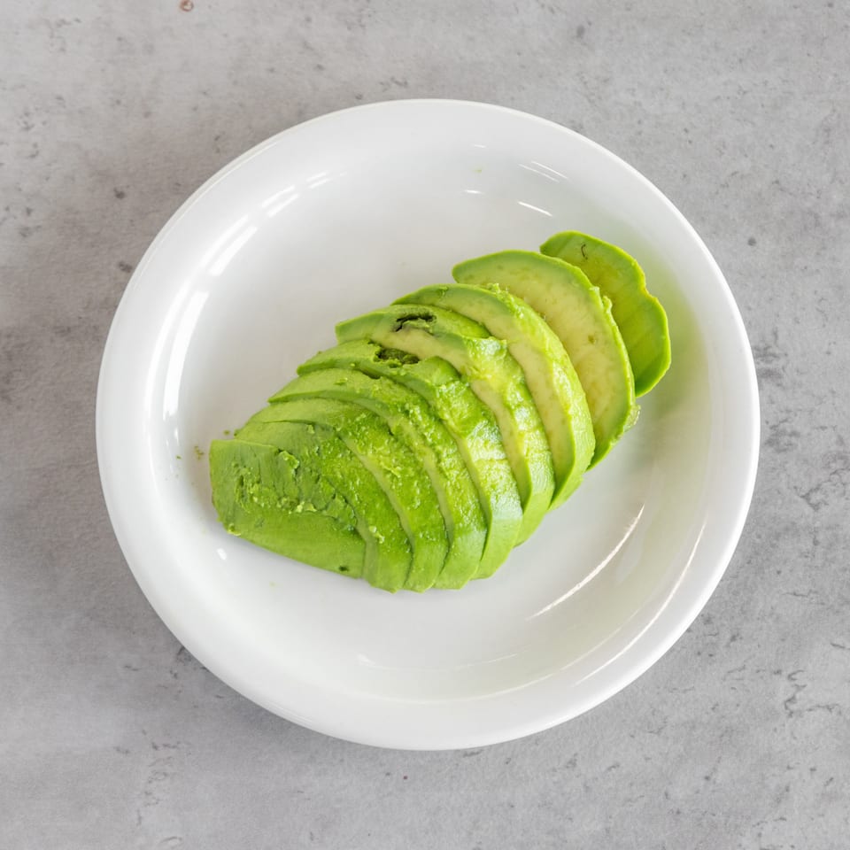 Sliced avocado arranged on a white plate atop a gray stone surface.