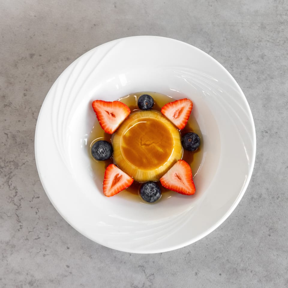 Stacked pancakes topped with syrup, sliced strawberries, and blueberries on a white plate.