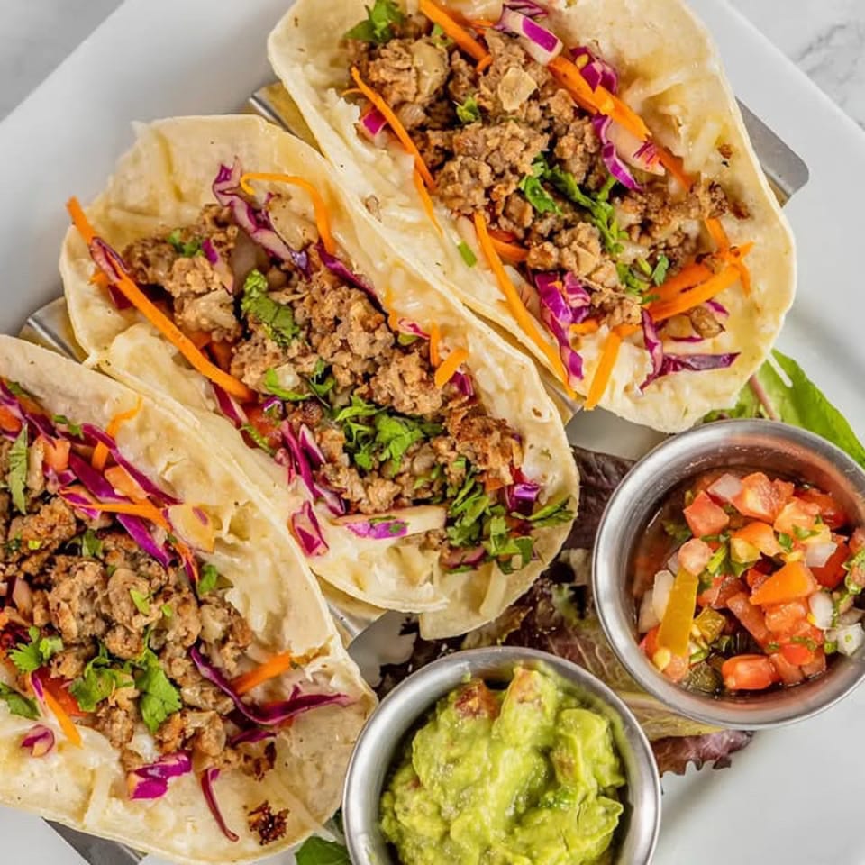 Three soft tacos filled with seasoned meat, cabbage, carrots, and cilantro, served with guacamole and pico de gallo.