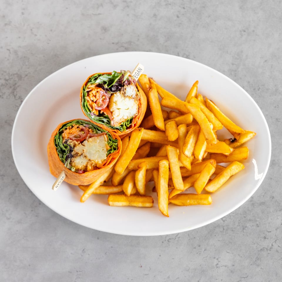 Two vegan vegetable wraps, sliced to reveal greens and tomatoes, served with golden French fries on a white plate.