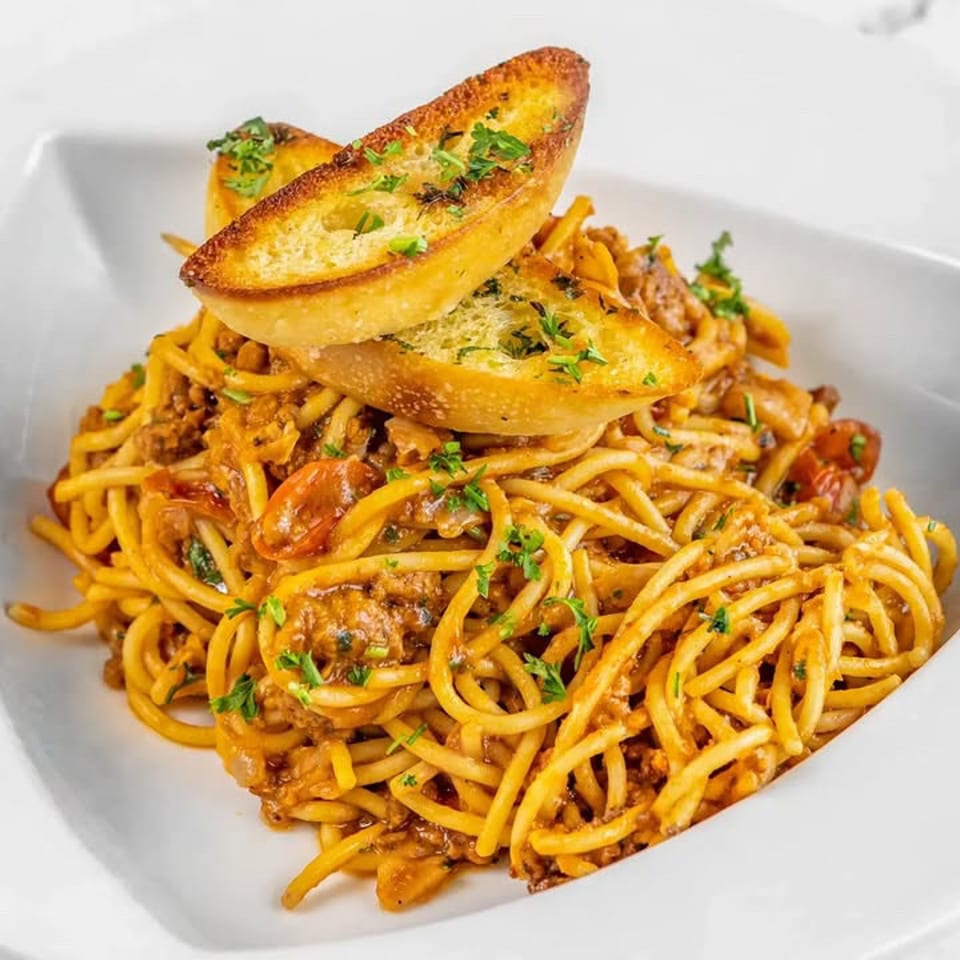 Spaghetti with meat sauce, shrimp, and herbs topped with toasted garlic bread in a white bowl.