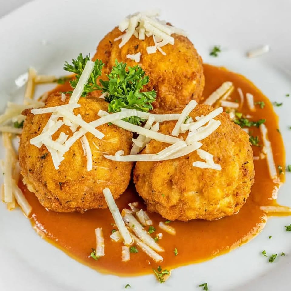 Three golden breaded meatballs served in tomato sauce, topped with shredded cheese and parsley on a white plate.