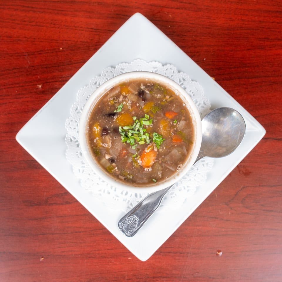 Bowl of vegetable soup garnished with fresh herbs, served on a white plate with a spoon atop a wooden table.