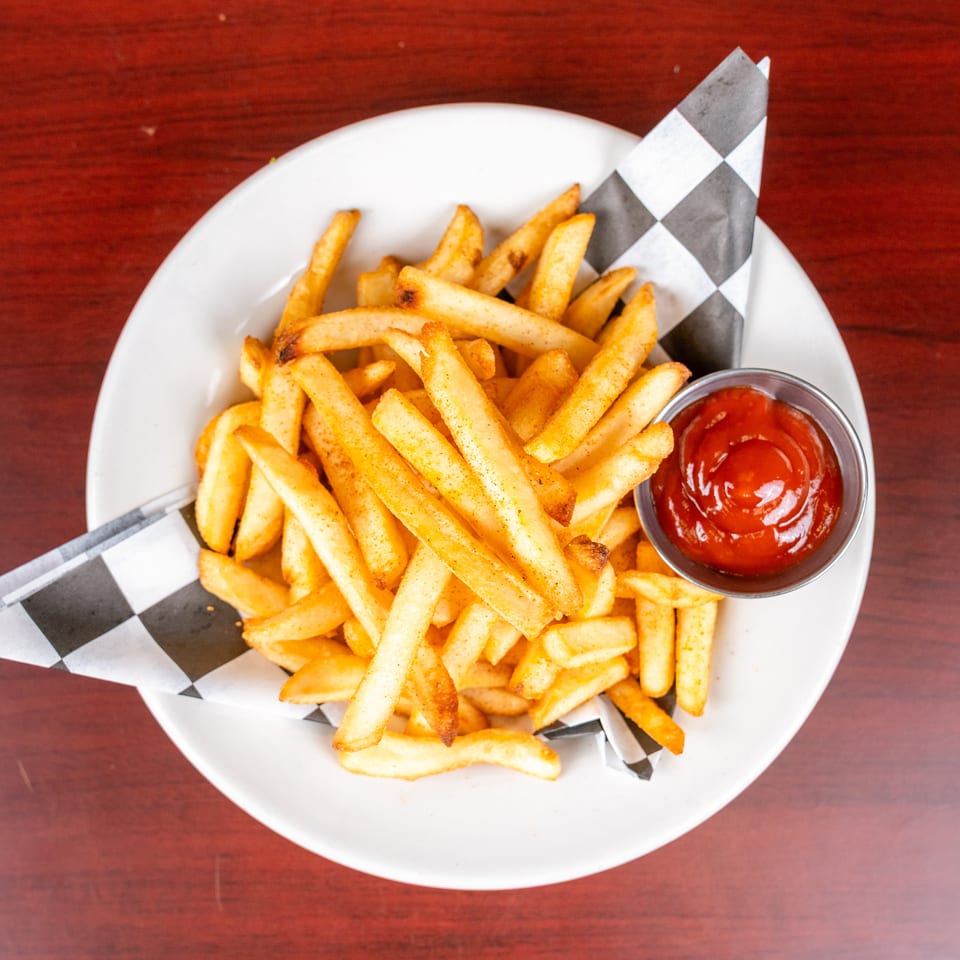 Crispy golden french fries served on checkered paper with ketchup in a metal cup on a white plate.