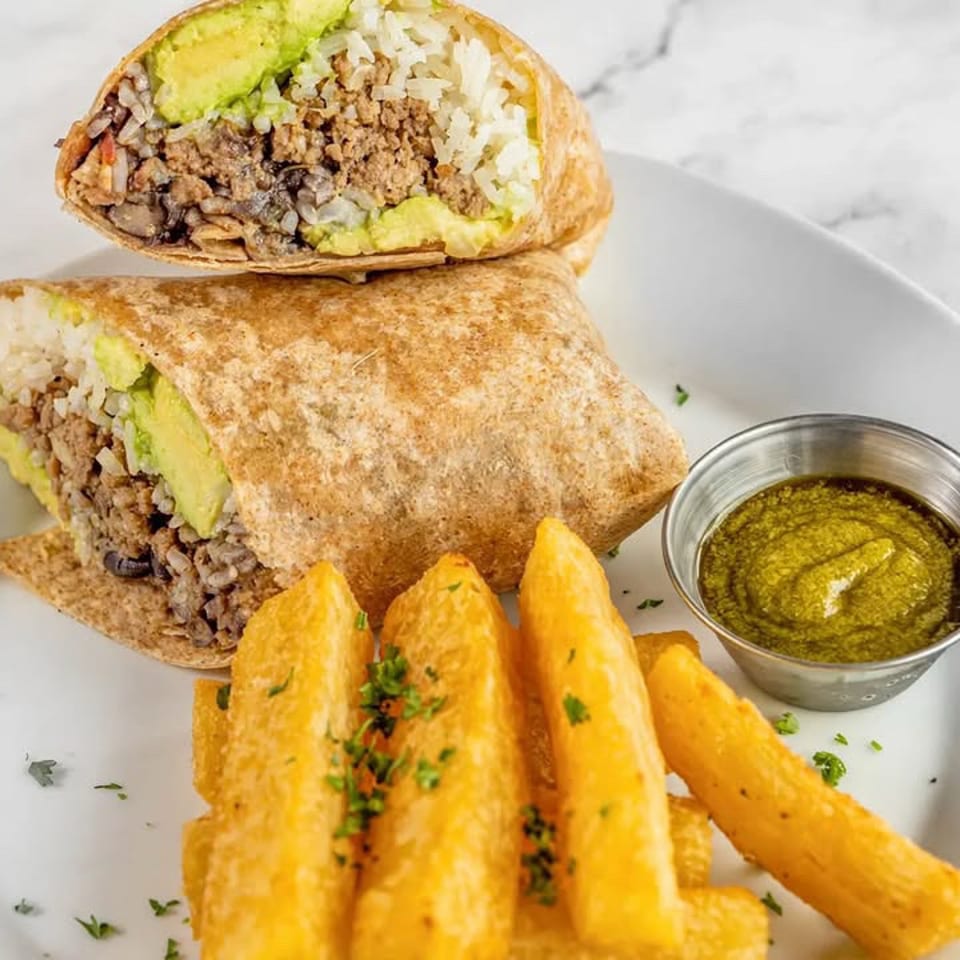 Sliced burrito filled with rice, beans, ground meat, and avocado, served with seasoned fries and green dipping sauce.