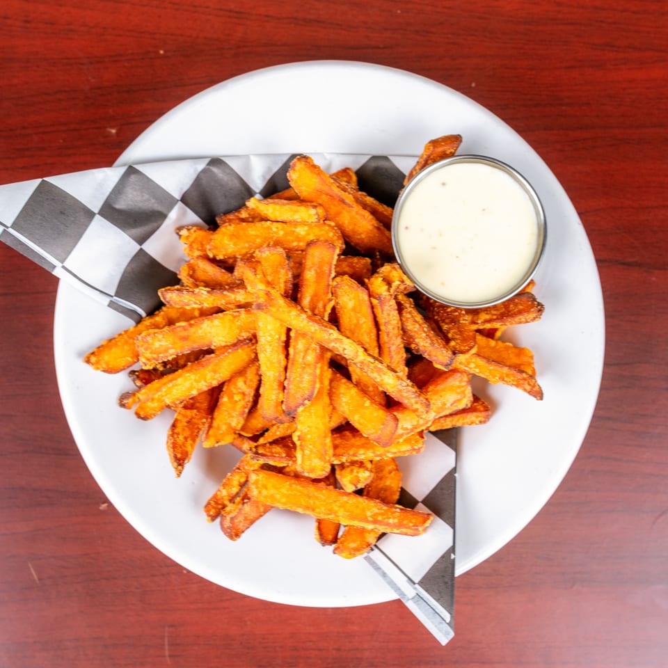 Crispy sweet potato fries served with creamy dipping sauce on a checkered paper-lined plate.