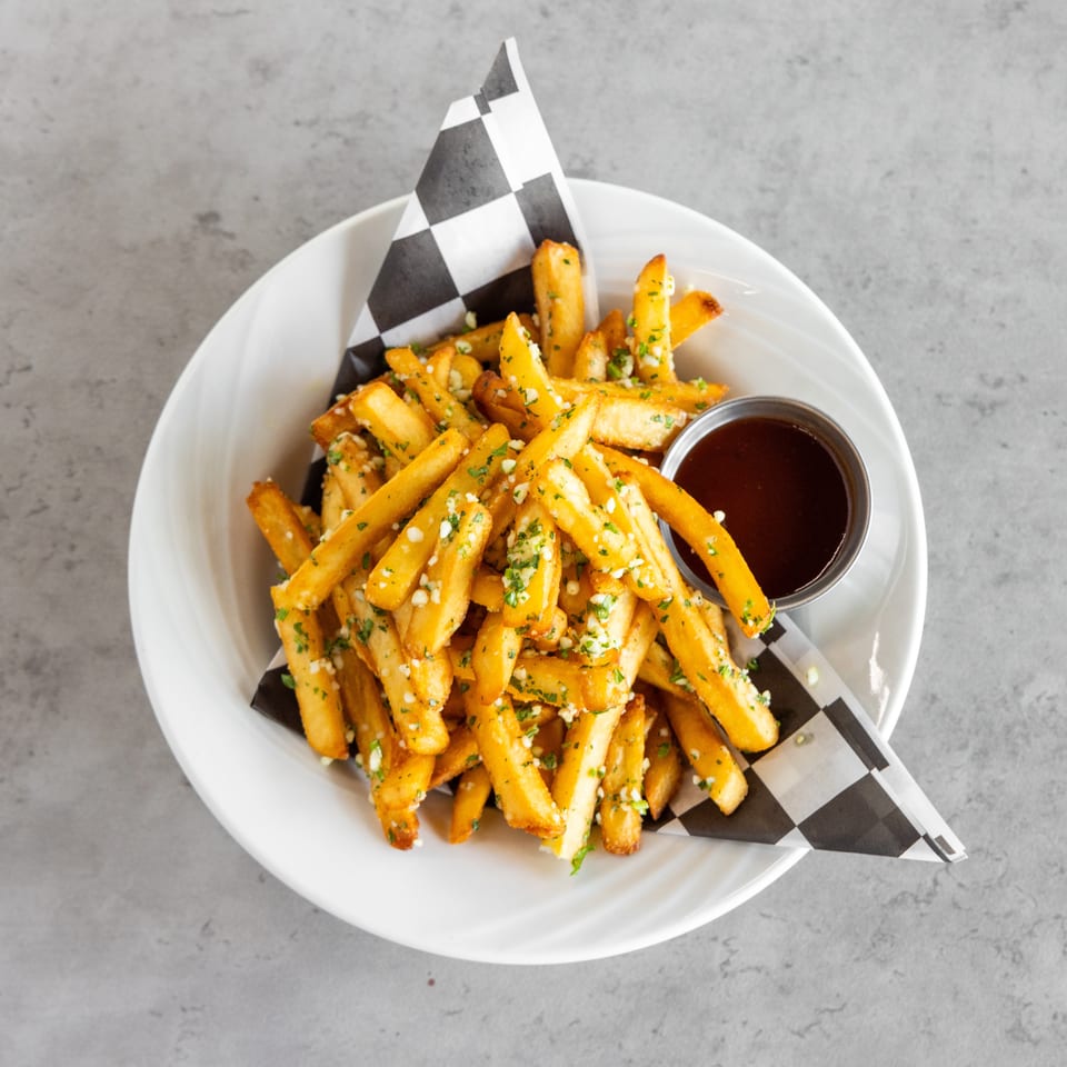 Golden garlic-and-herb fries piled in a bowl with a side of dark dipping sauce.