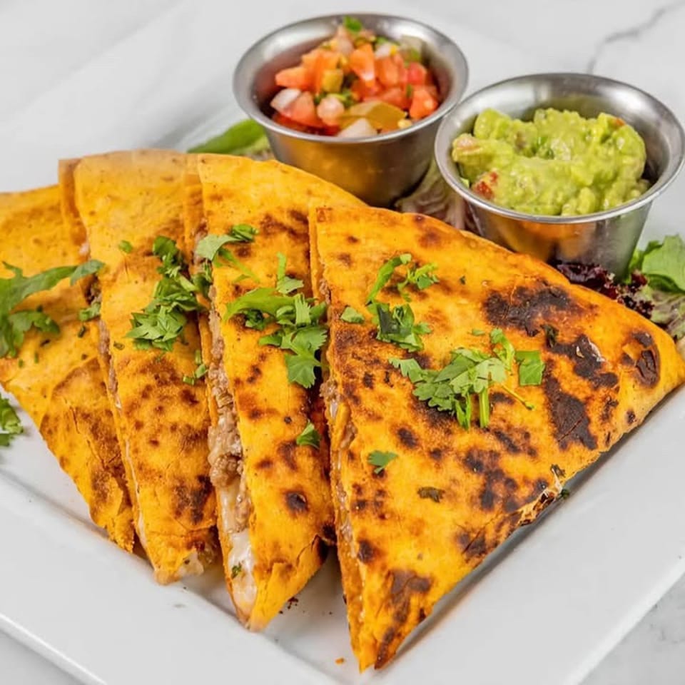 Grilled golden quesadilla wedges topped with cilantro, served with guacamole, pico de gallo, and lettuce on a white plate.